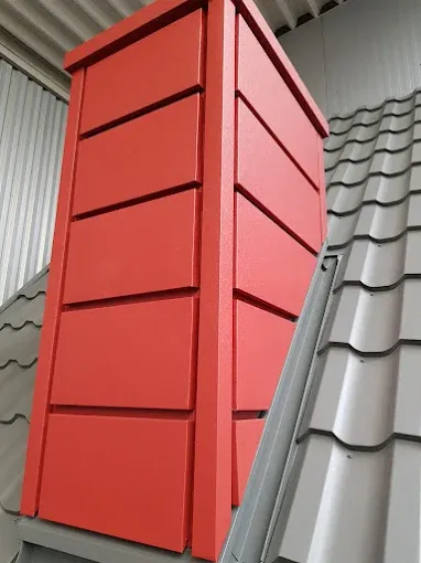 Komin obłożony czerwoną blachą płaską z obróbką przy grafitowej blachodachówce