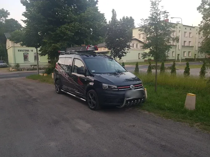 Oznakowany samochód firmowy Komplex-Dach z drabiną na dachu, zaparkowany na osiedlu